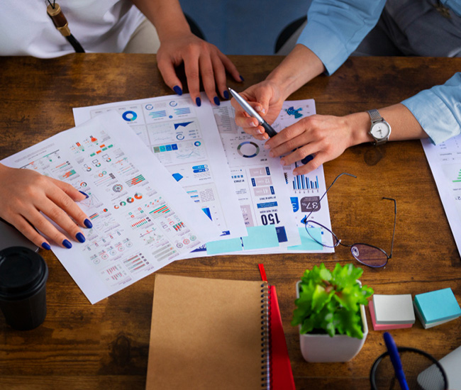 A person uses a laptop displaying a website builder interface, with a smartphone and tablet showing the same website design; green plants are visible at the top corners of the workspace. A person uses a laptop displaying a website builder interface, with a smartphone and tablet showing the same website design; green plants are visible at the top corners of the workspace.