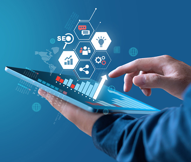 A person uses a laptop displaying a website builder interface, with a smartphone and tablet showing the same website design; green plants are visible at the top corners of the workspace.